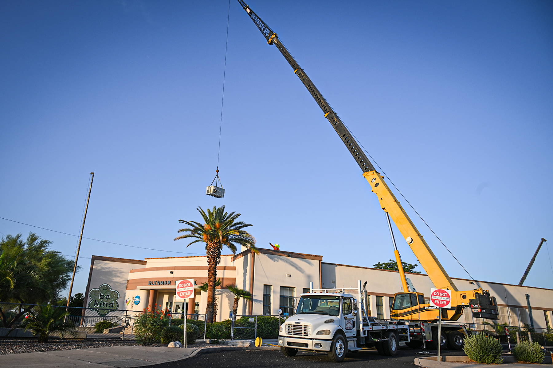 A crane lowers an air conditioner onto the roof of Blenman Elementary