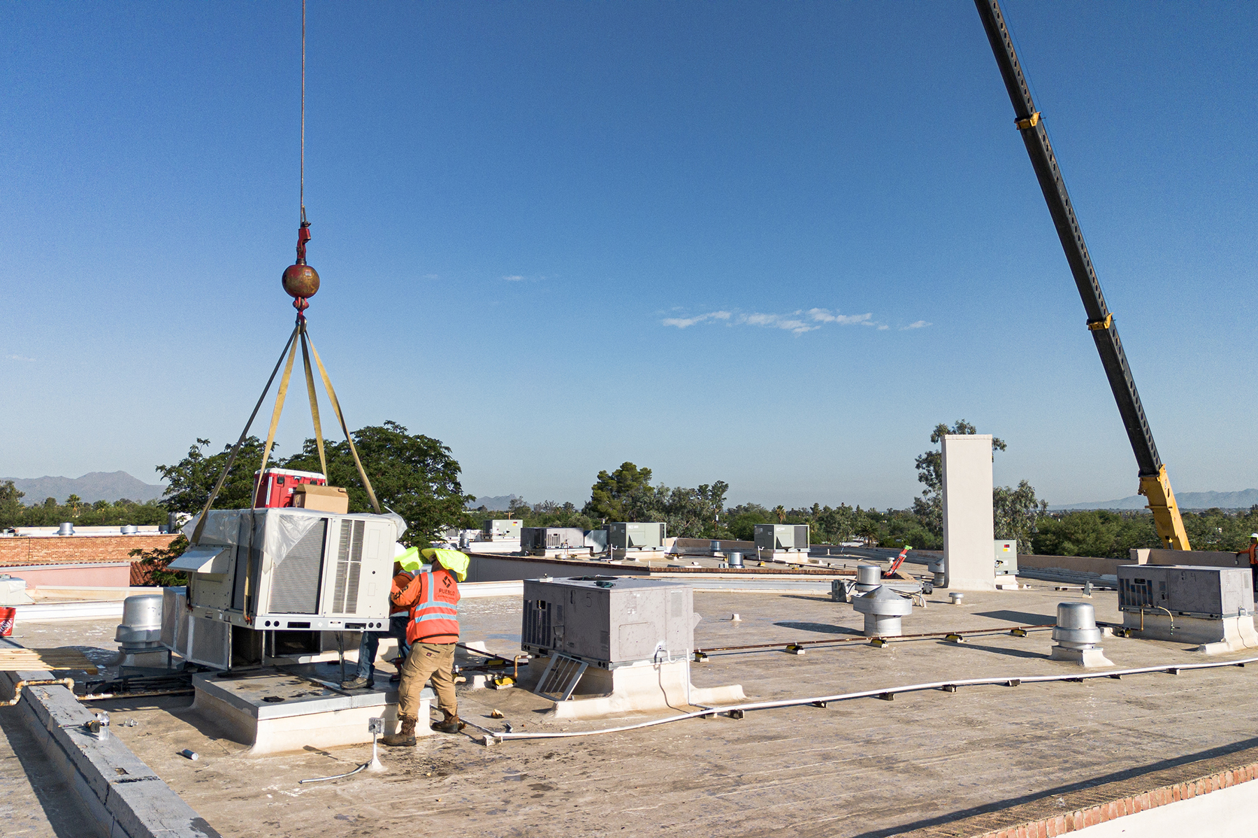 HVAC workers in safety gear lower an air conditioner into its place on the roof