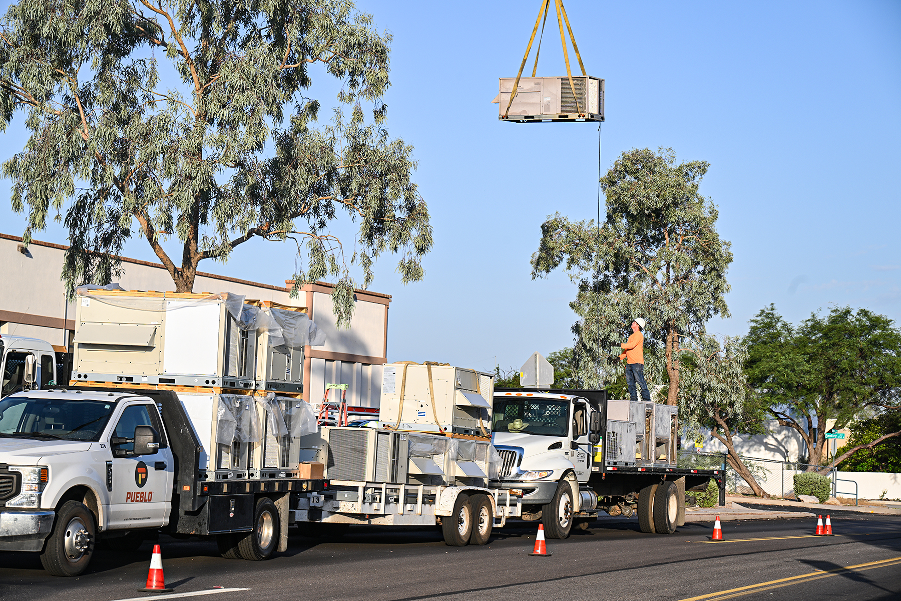 An HVAC worker helps raise an air conditioner into the crane