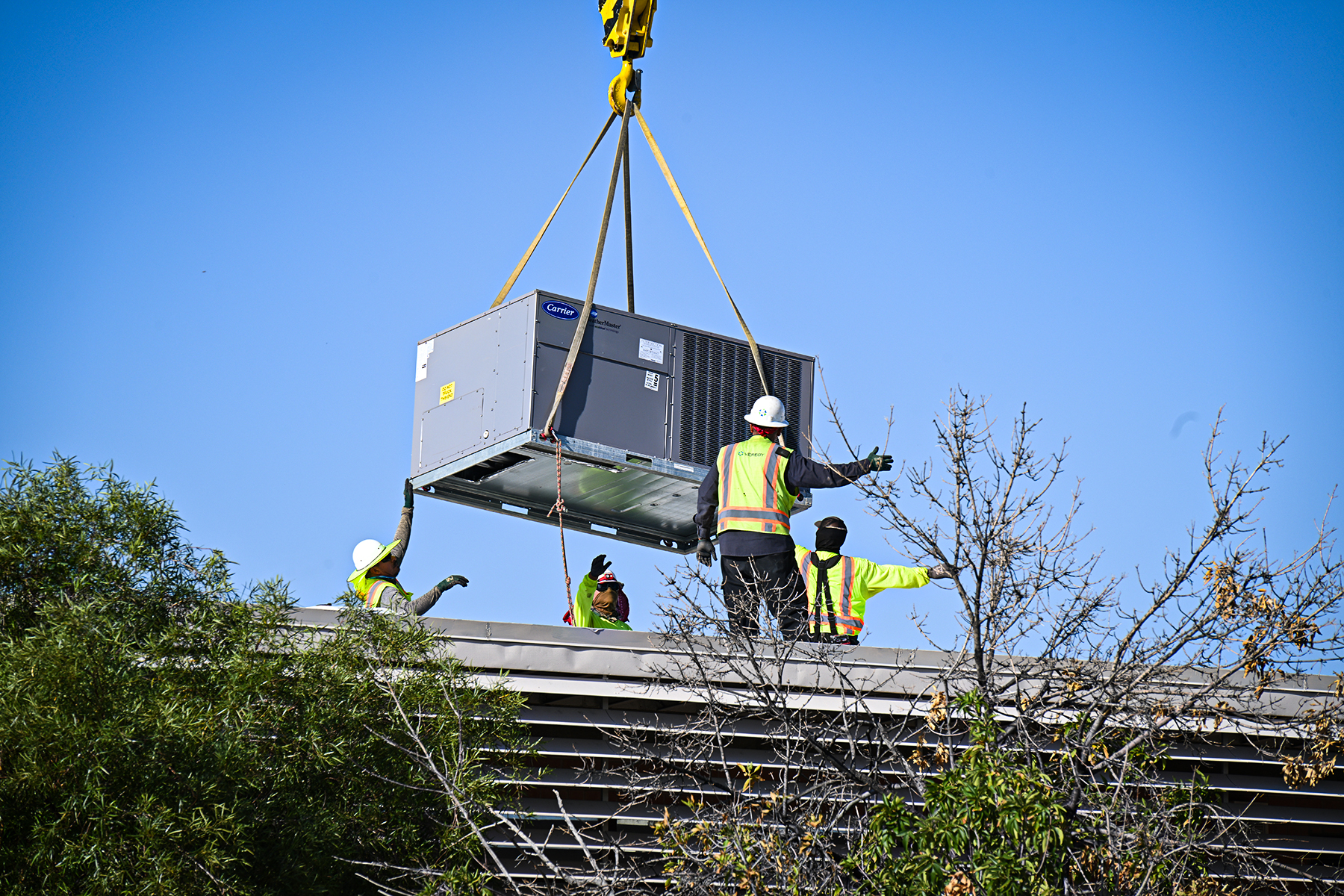 HVAC workers stand on the roof lowering an air conditioner into place