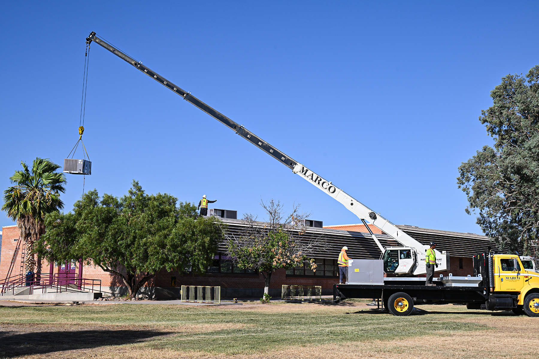 A crane lowers an air conditioner onto the roof of Bonillas