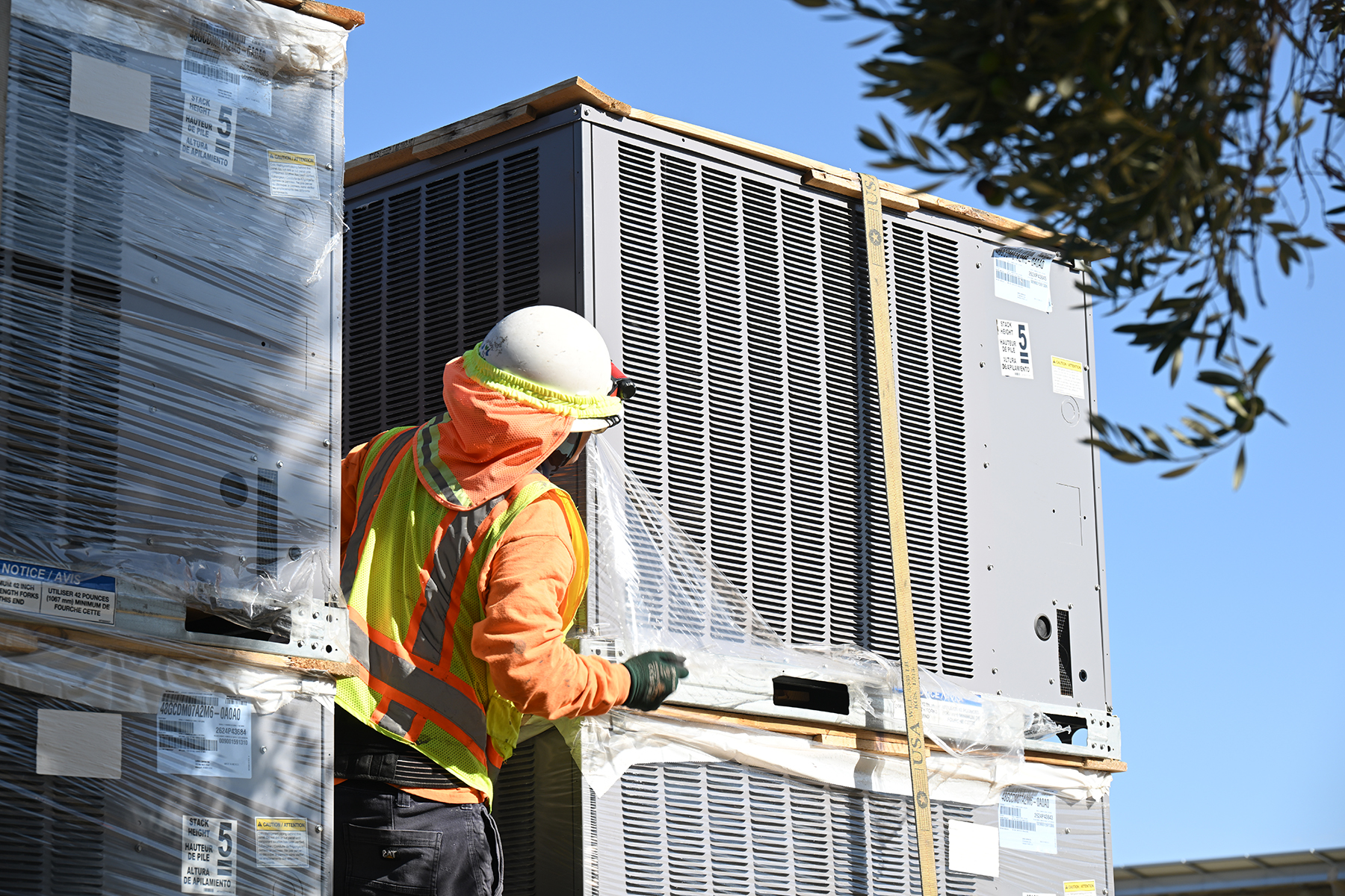 An HVAC worker in safety gear positions an air conditioner on the roof