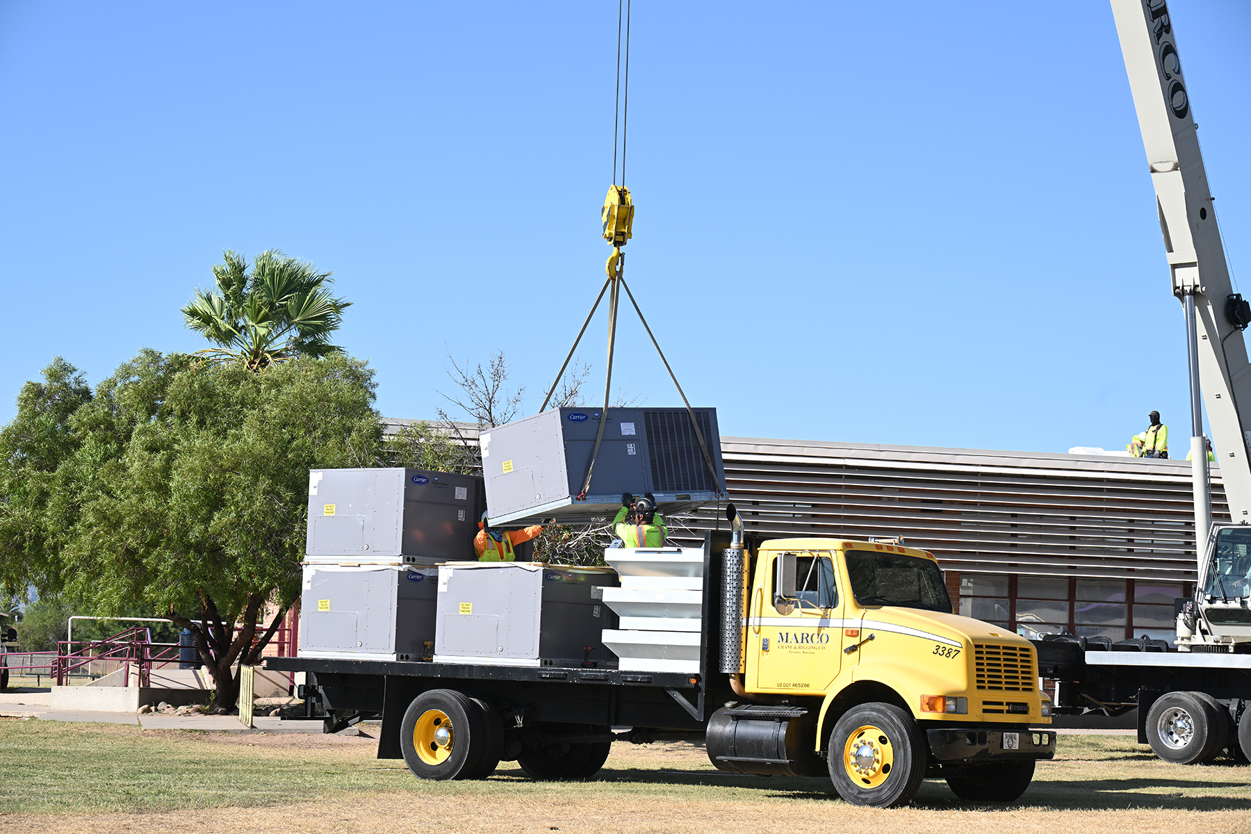 A crane lifts an air conditioner from a work truck