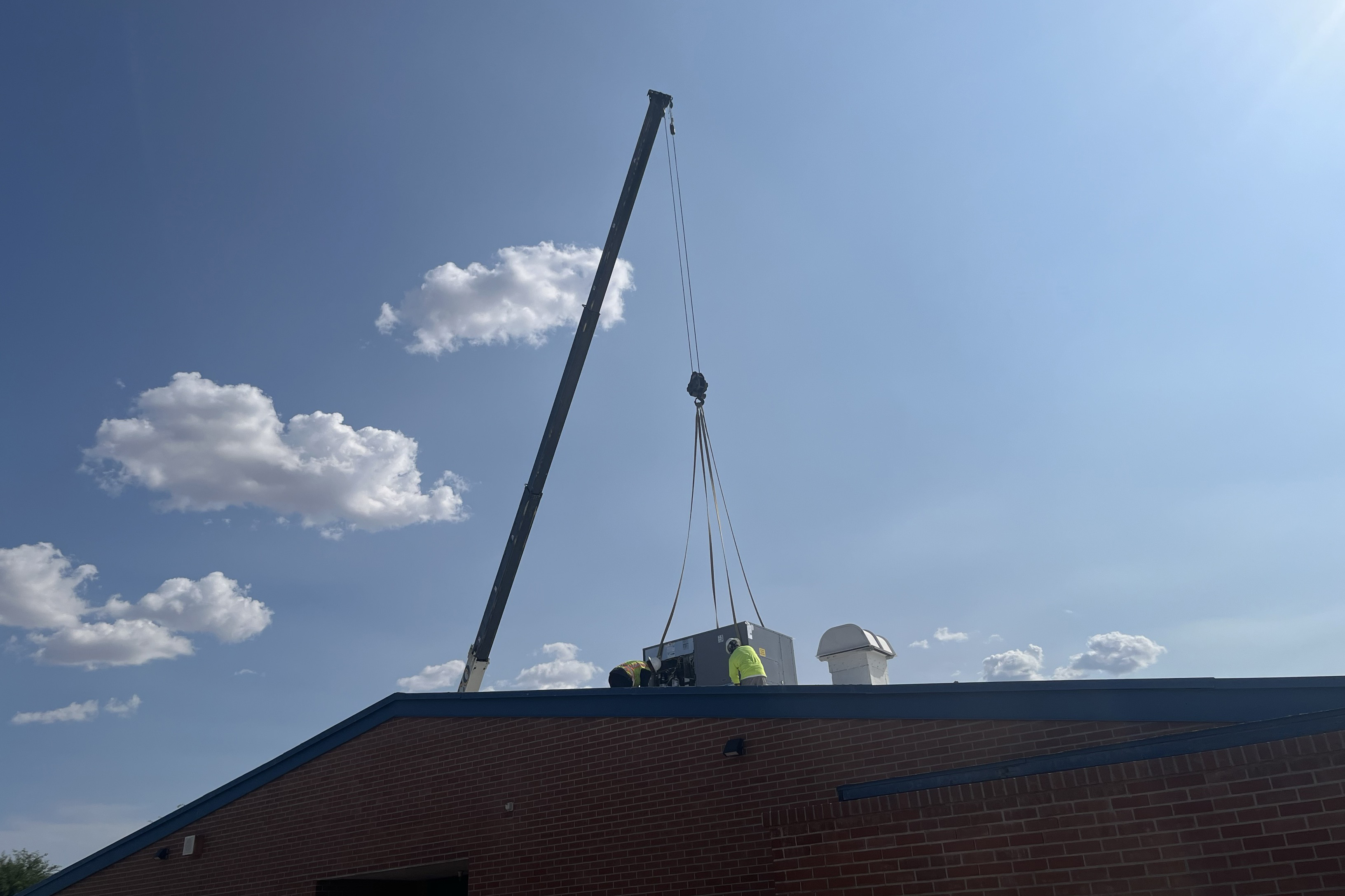 A crane lowers an air conditioner onto the roof of Cavett Elementary