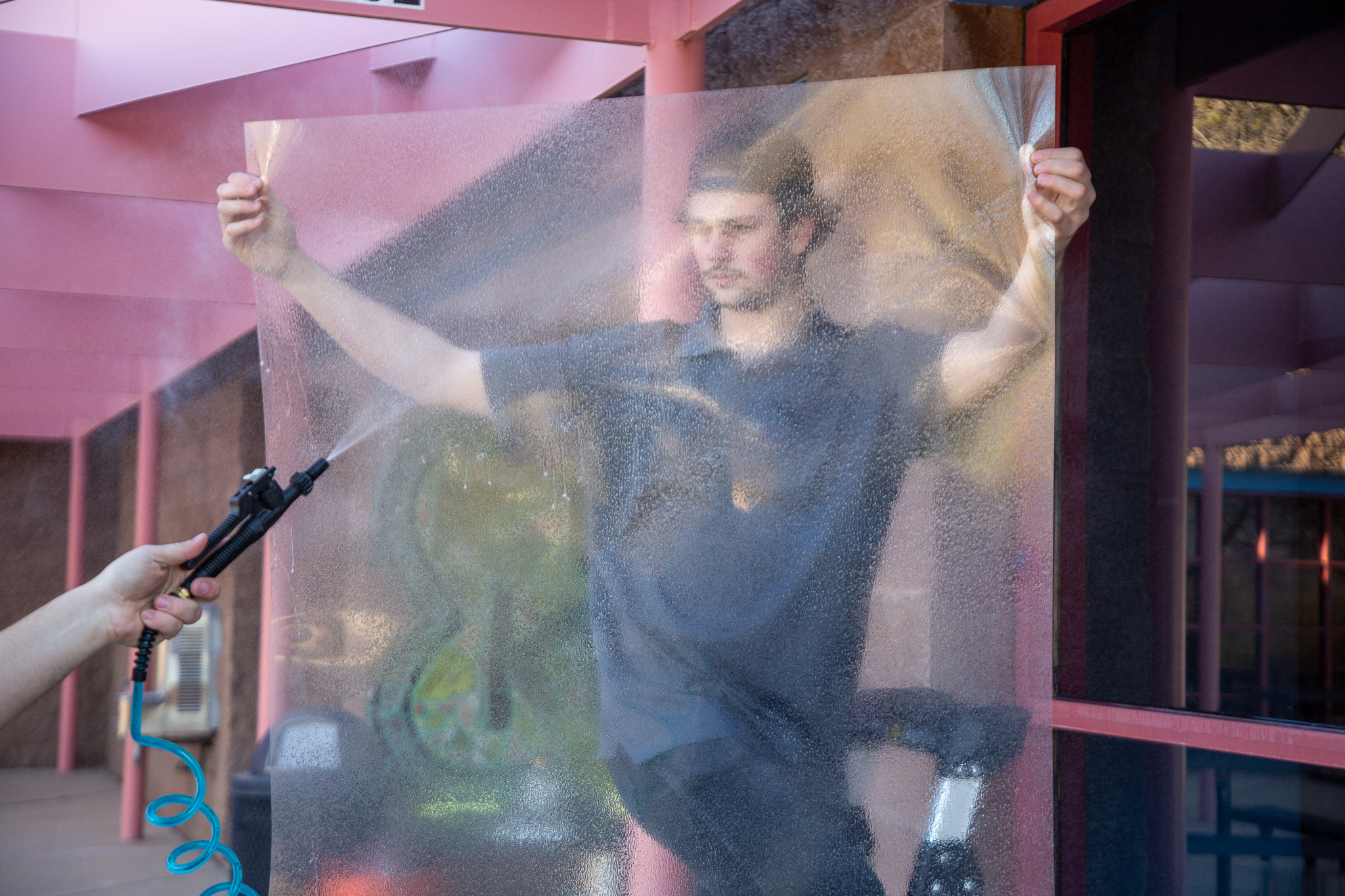 A man holds up a security film while another man sprays it with water