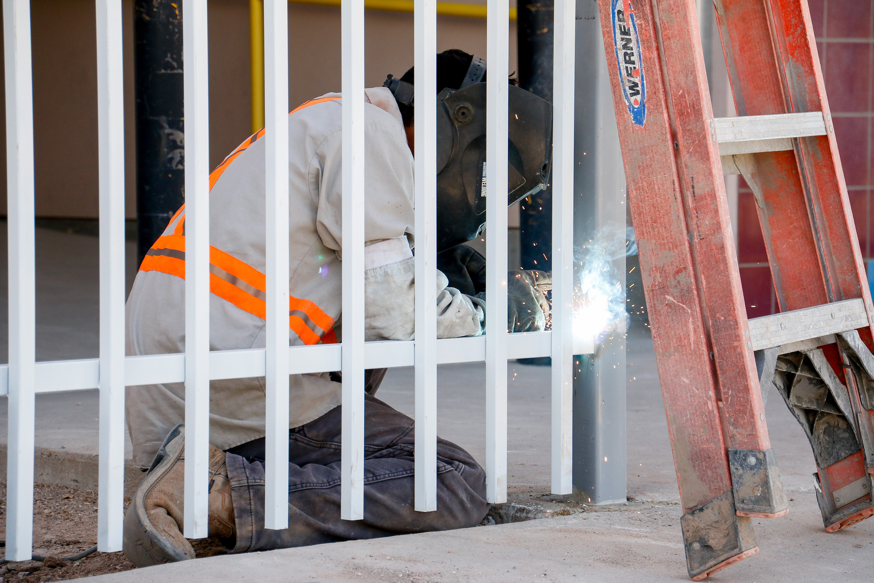 A man in a safety mask uses welding tools on a gate