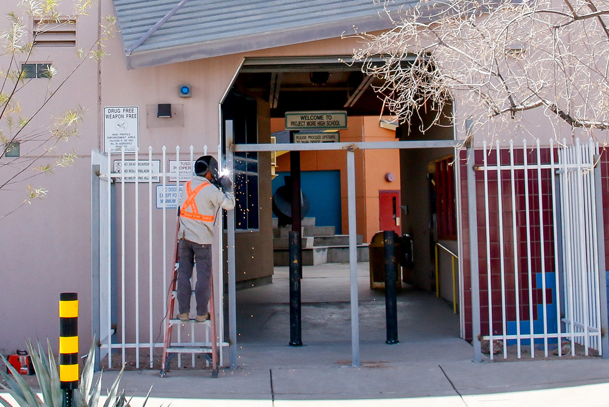 A man stands on a ladder welding a gate