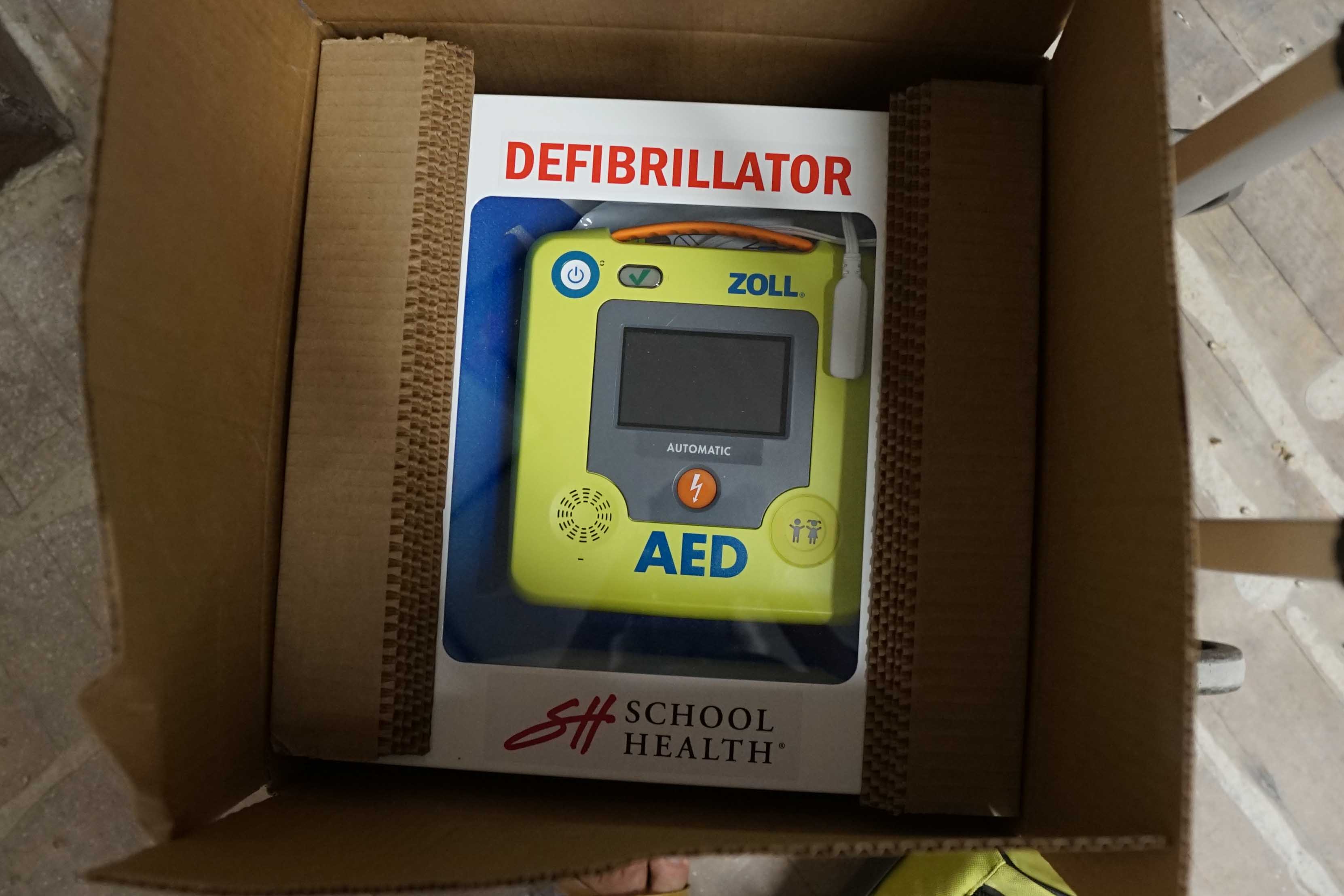 A bright green defibrillator sits in its packaging