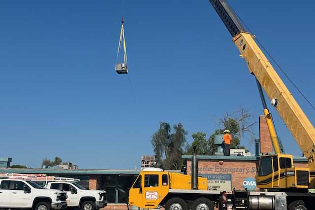 A yellow crane lowers an air conditioner onto Wheeler