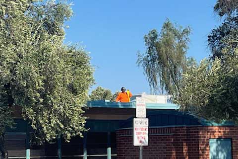 An HVAC worker wearing orange safety gear stands on the roof